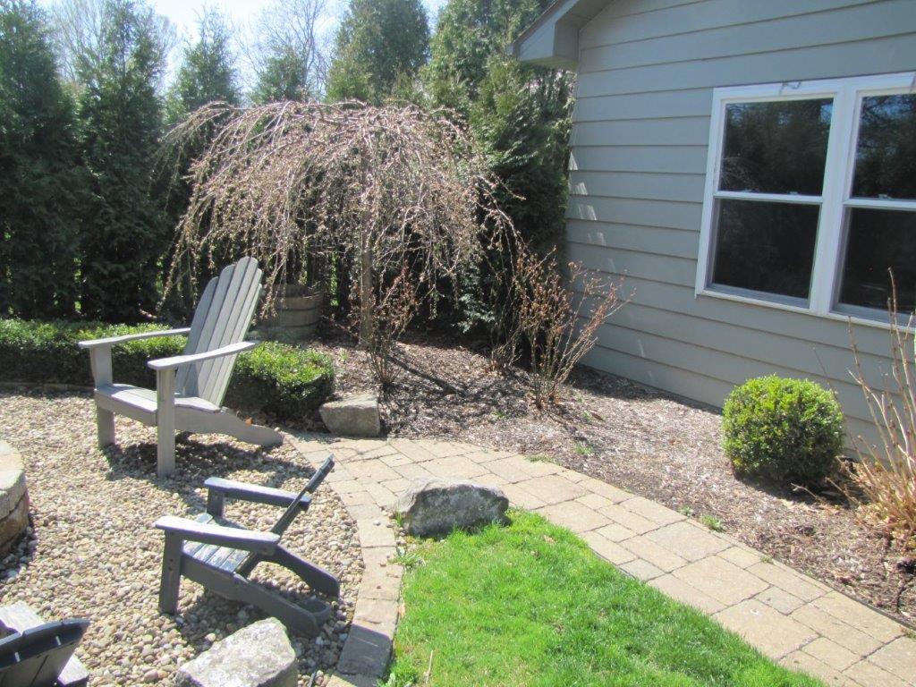 Backyard patio with chairs, brick pavers, green lawn, shrubs, and a house exterior