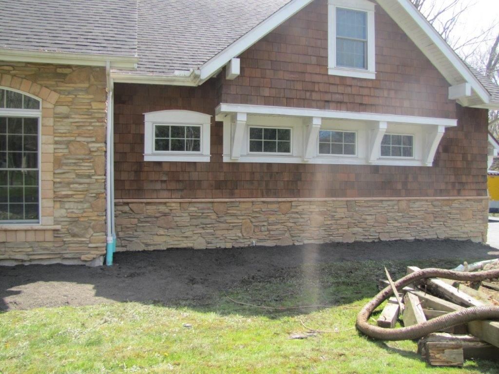House exterior with brown siding, white-trimmed windows, and a pile of debris in the yard