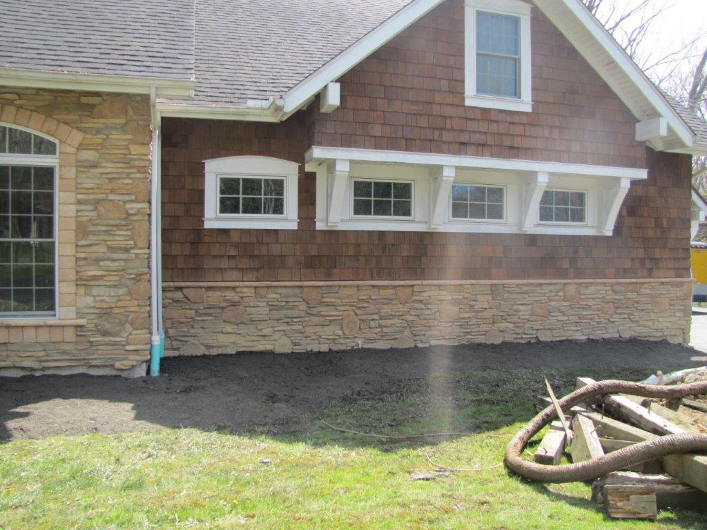 Brick house exterior with tan siding, white-trimmed windows, and dark soil landscaping in front.