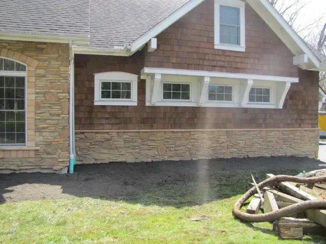 House exterior with stone and shingle siding, white-trimmed windows, and a bare dirt foundation border