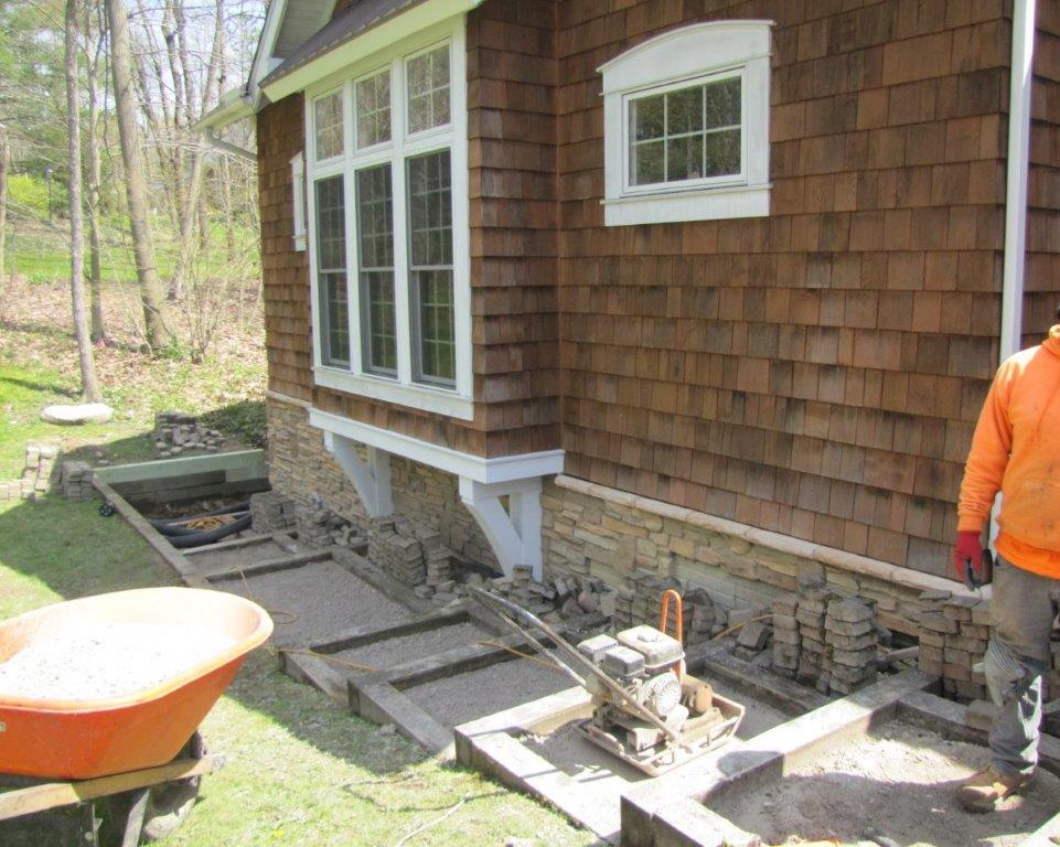 House exterior with shingled siding and windows under construction, with materials and a worker at right