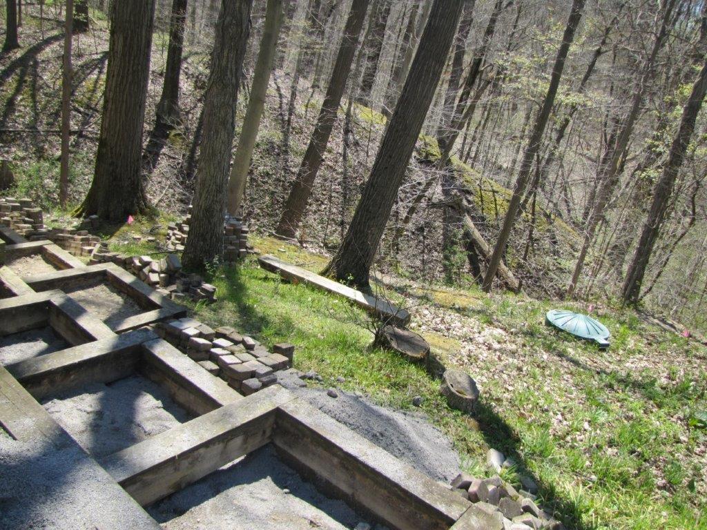 Wooded hillside with a concrete stepped structure and scattered logs beside a grassy path