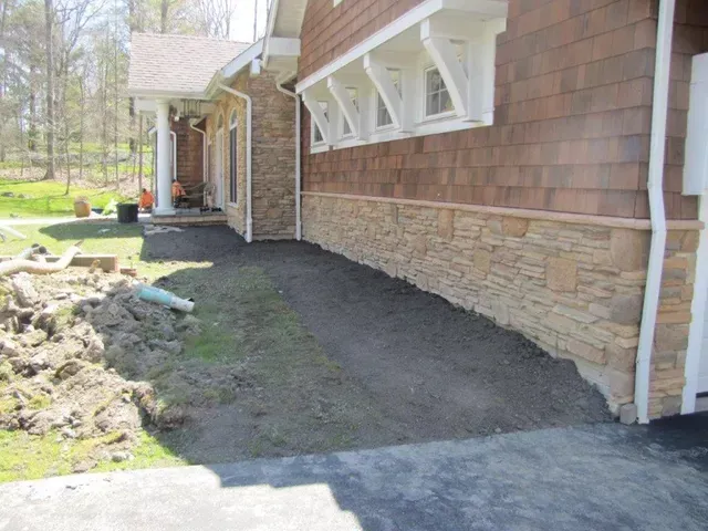 House exterior with newly landscaped dirt strip along the foundation and white awning supports