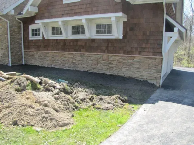 House exterior with white-trimmed windows, stone base, and a dirt pile along the front yard