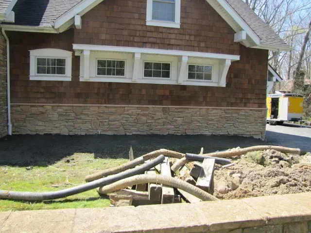 House with damaged foundation and exposed pipes beside a dirt excavation area