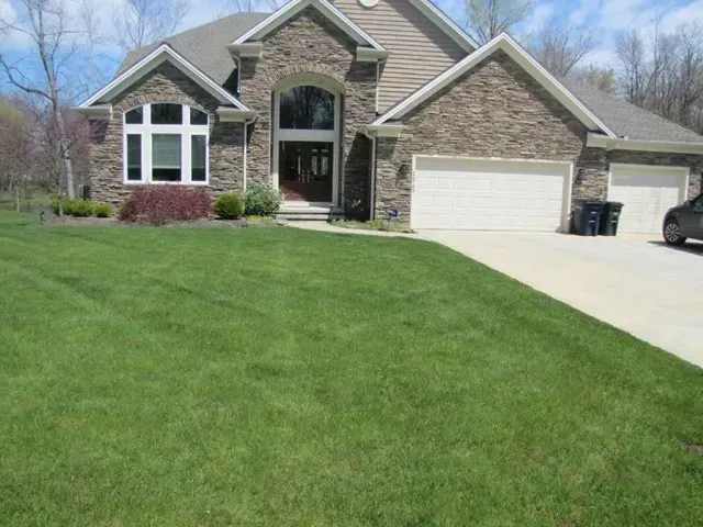 Brick suburban house with a green lawn, front porch, and two-car garage under a clear sky