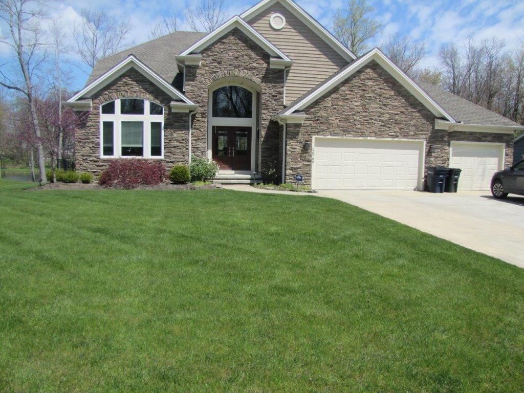 Suburban brick house with three-car garage, stone accents, and a large green lawn under a clear sky