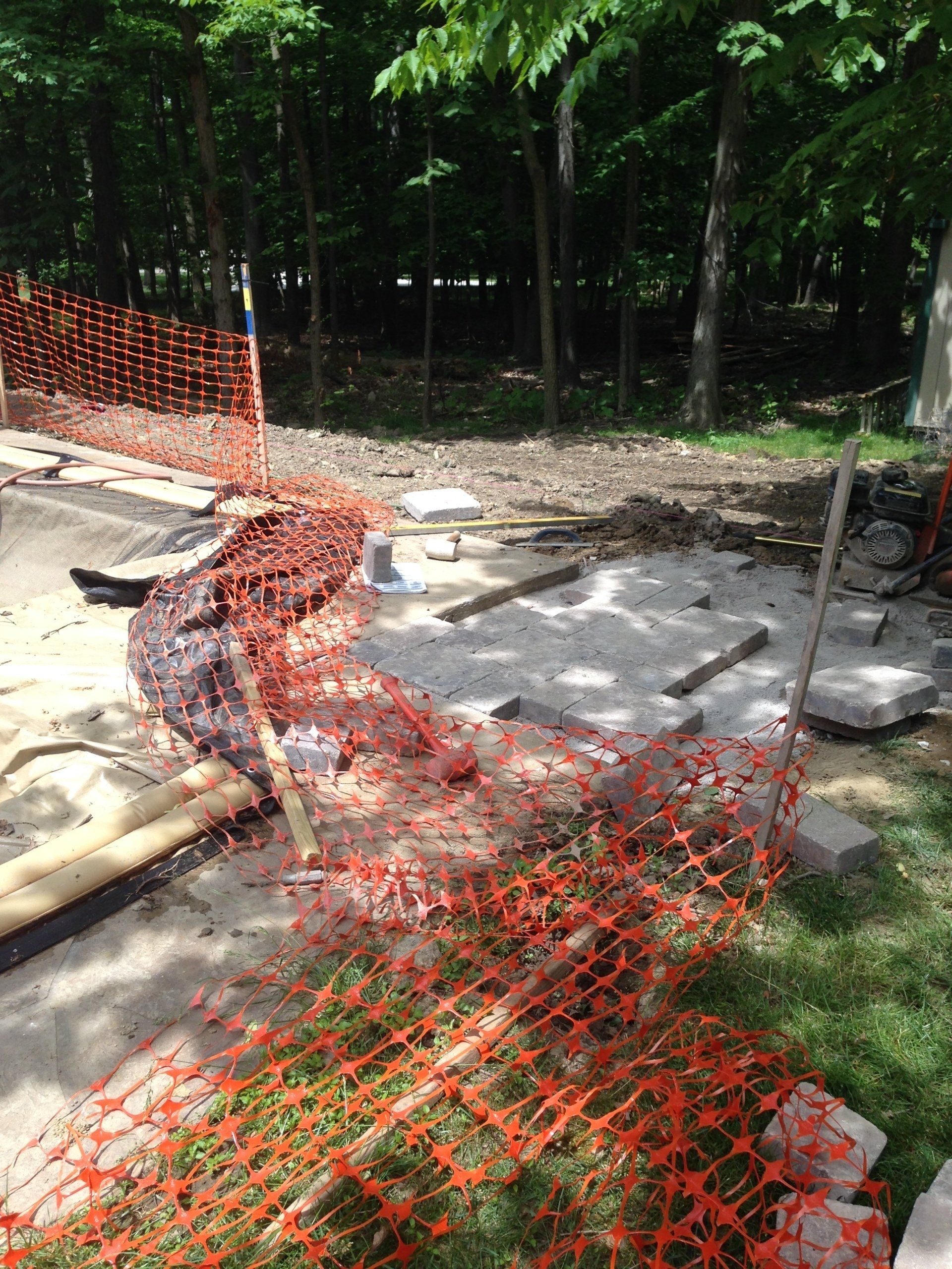 Orange safety netting around a construction area beside a wooded path
