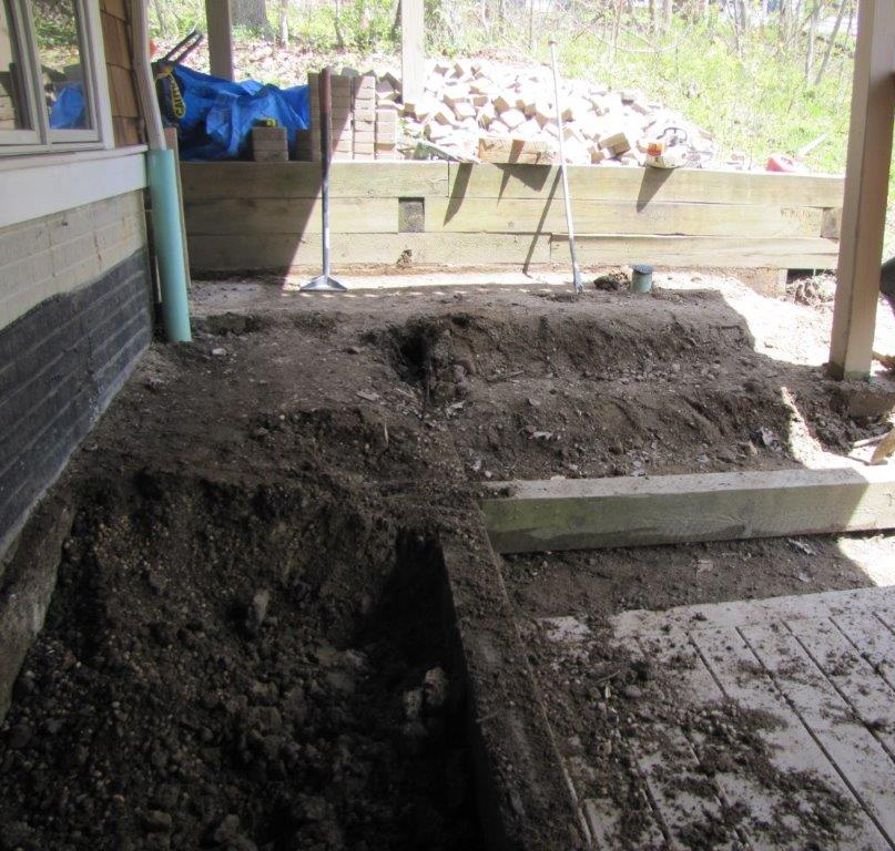 Dug-up backyard beside a house, with piles of soil, concrete steps, and a small retaining wall under construction