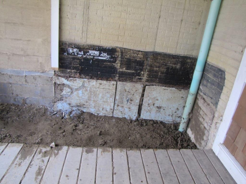 Damaged exterior wall with black water stains and chipped plaster above a concrete floor and deck boards