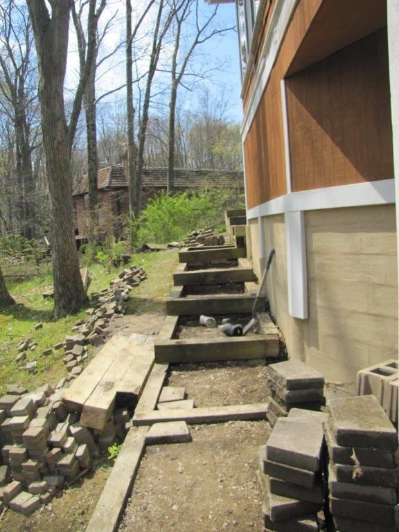 Steep outdoor staircase with concrete steps beside a house, bordered by trees and a rocky yard.