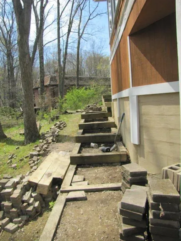 Wooden steps and retaining walls beside a house on a dirt slope in a wooded yard