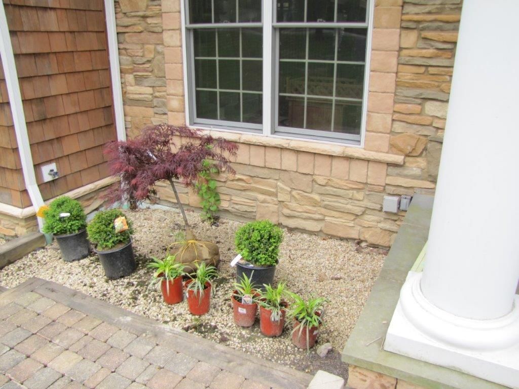 Front porch garden with potted plants, a stone wall, and a white column beside brick pavers.