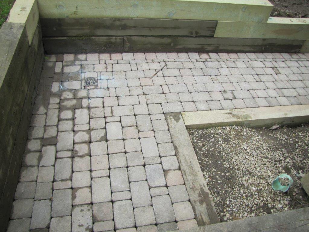 Paved courtyard with small stone tiles, concrete borders, and a gravel planting bed.