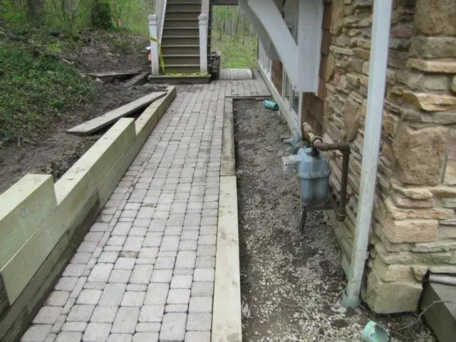Stone walkway beside a house, with steps ahead and a narrow gravel strip along the wall.