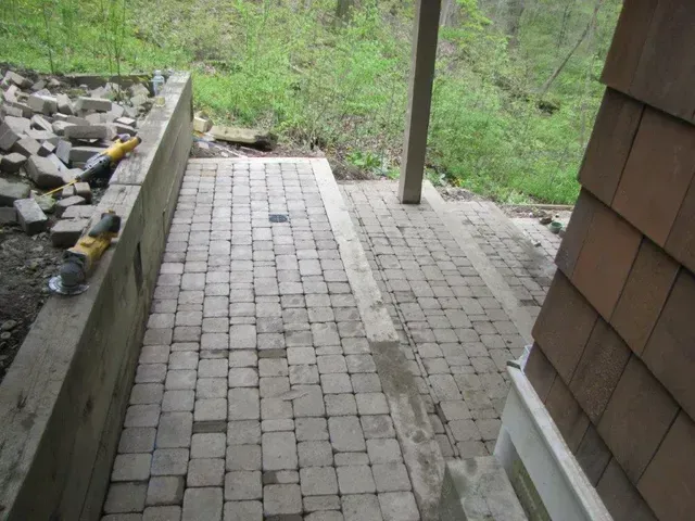 Stone-paved patio beside a rock-lined wall, leading down to a green wooded slope