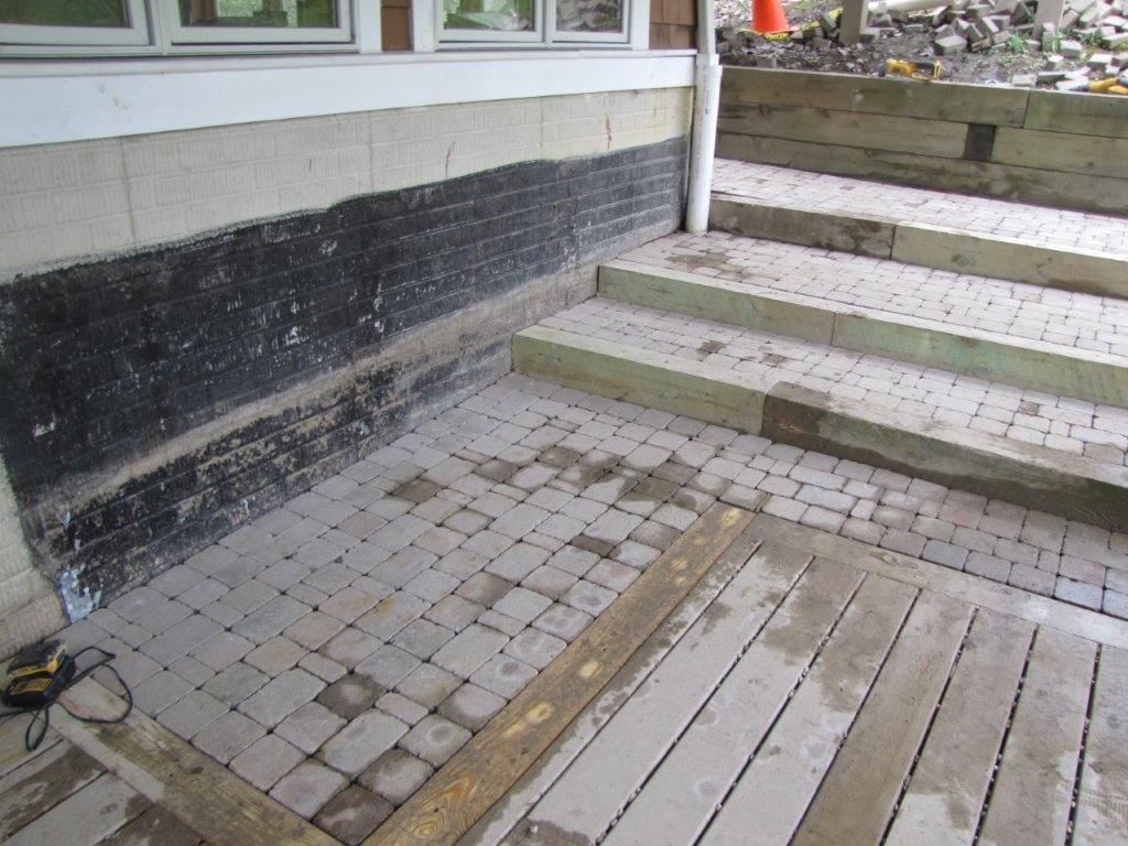 Paved steps and a tiled walkway beside a building, with a black-and-white wall and railing.