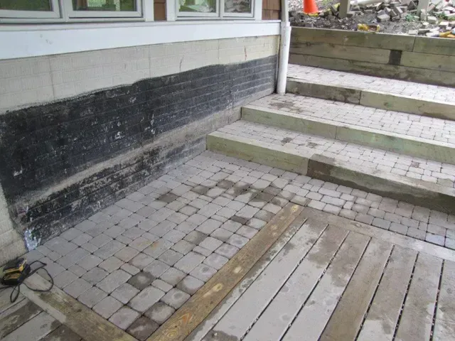 Stone steps and a worn paved walkway beside a building with a black-and-white wall.