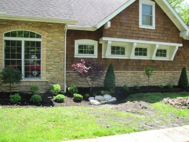 Front of a brick house with arched window, mulched flower bed, shrubs, and green lawn.
