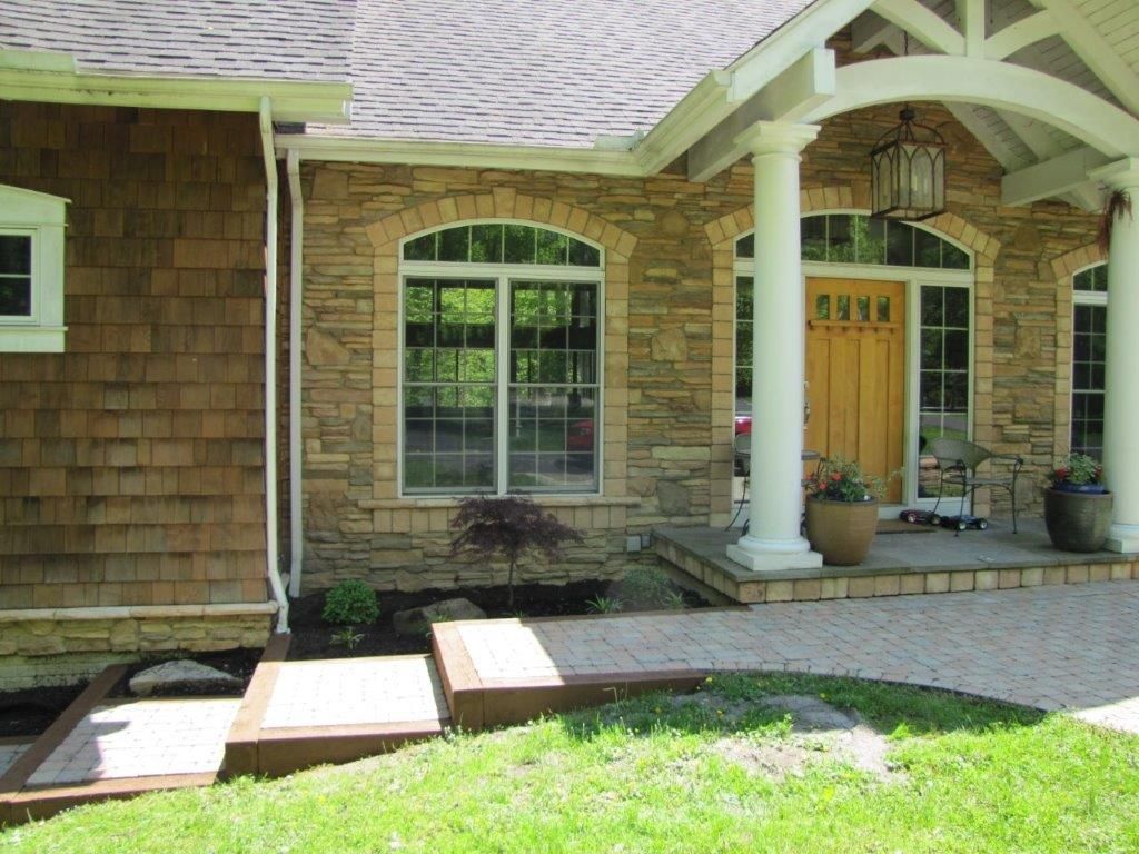 Front porch with stone siding, arched window, yellow door, white columns, and brick walkway.
