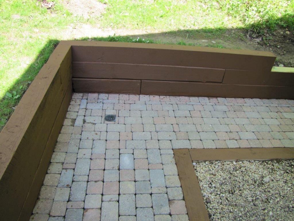 Backyard patio with brick pavers, low brown retaining walls, and a gravel corner bed