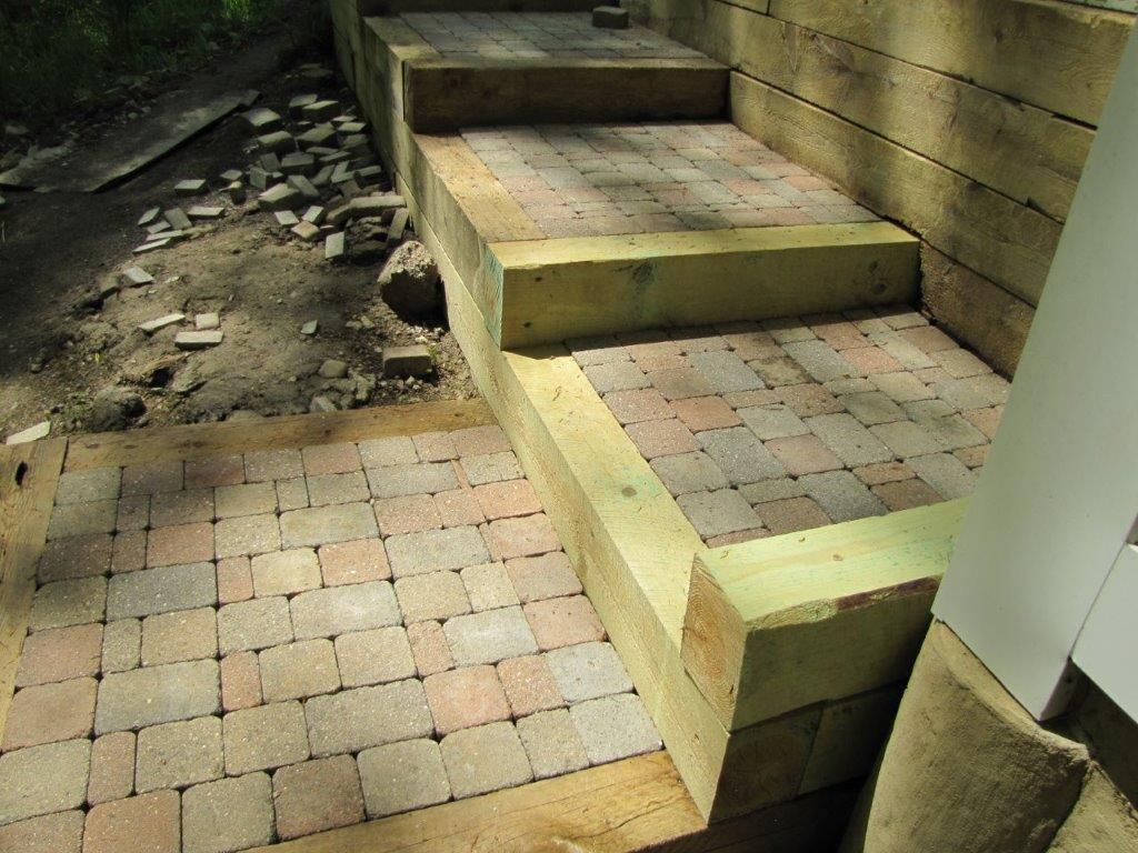 Stone steps in a backyard patio with brick pavers and a wooden retaining wall