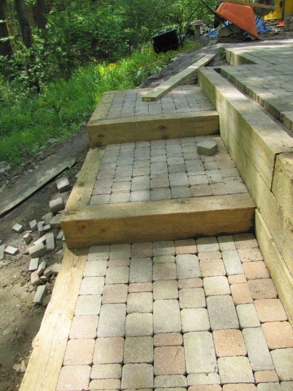 Stone steps with uneven brick paving on a sloped outdoor path beside greenery