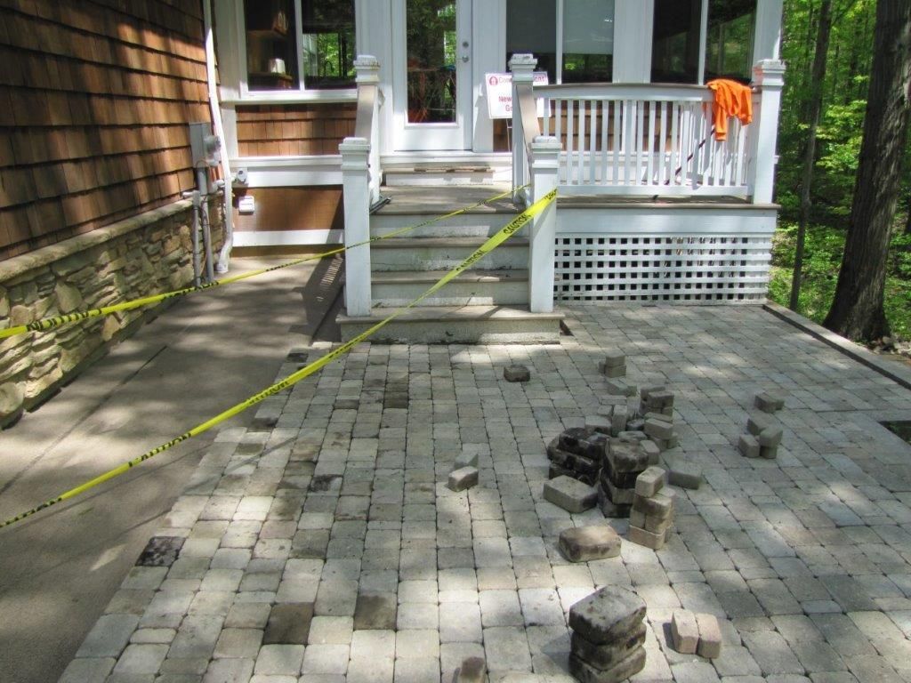 Front porch walkway with yellow caution tape and stacked pavers on a brick path.