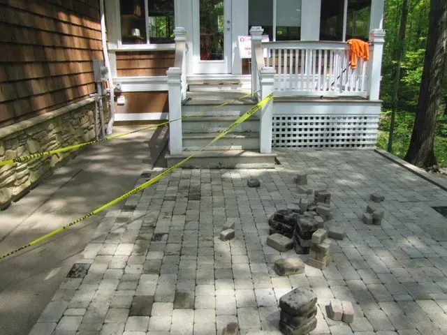Damaged brick walkway leading to a porch, with yellow caution tape and scattered debris along the path