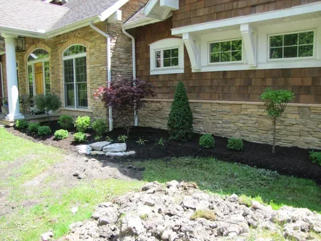 Front yard landscaping with mulch beds, shrubs, and stone accents beside a brick house