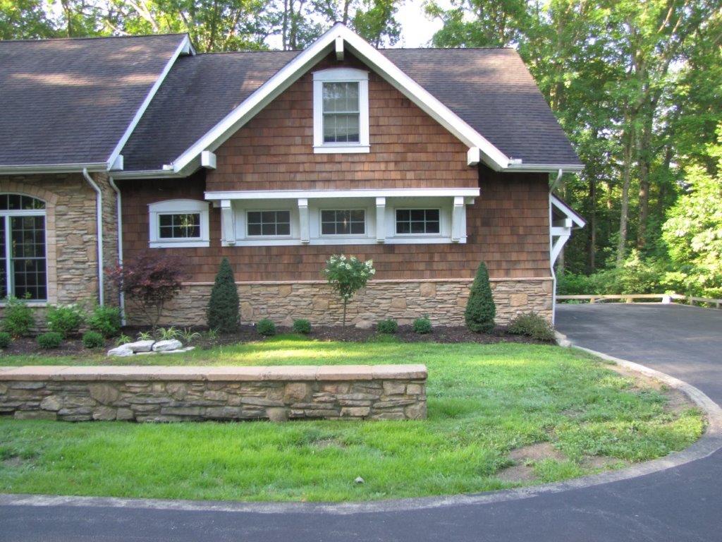 Brick house with tan gable, white trim, stone planter, and curved driveway beside green lawn