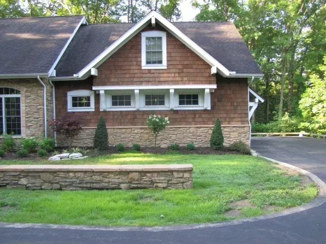 Brick house with dark roof, stone planter, and curved driveway beside a green lawn.
