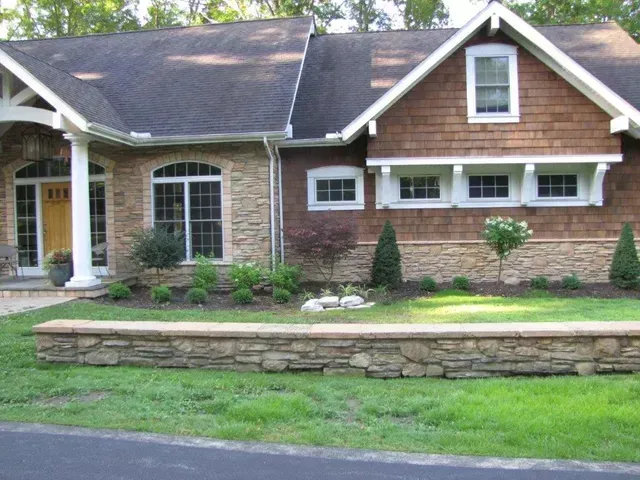 Brick house with dark roof, white trim, arched windows, and a stone retaining wall in front