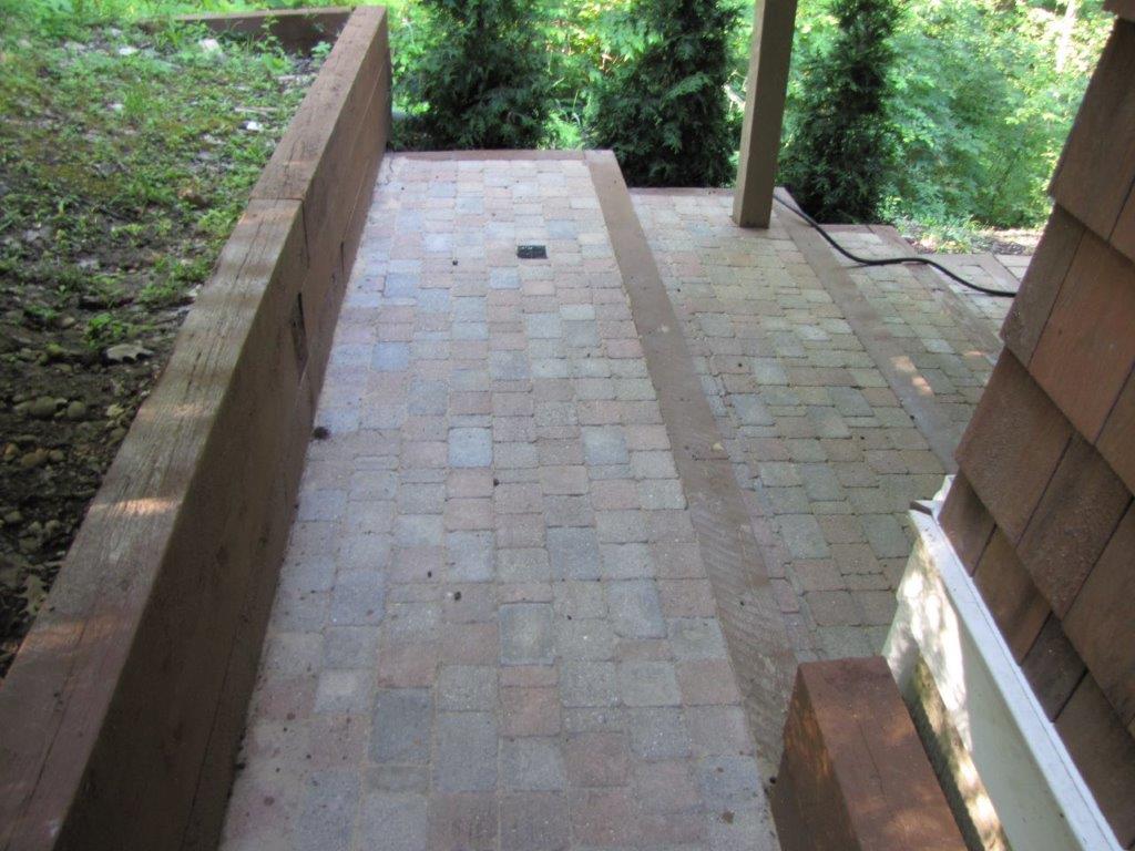 Brick walkway with a ramp leading down between stone walls and greenery.