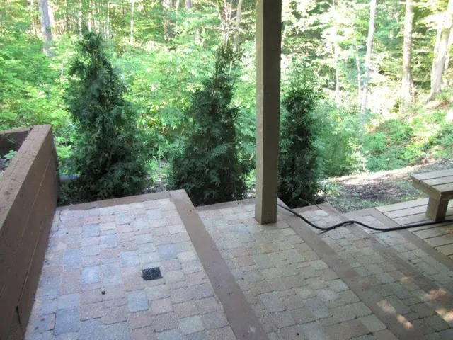 Patio with brick steps, a bench, and a wooden post overlooking a green wooded area