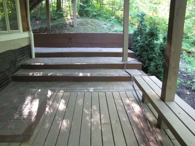 Wooden porch with steps, railing, and bench overlooking a wooded backyard.