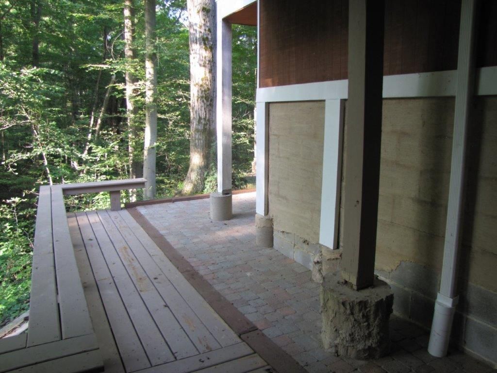 Wooden porch deck beside a rustic cabin, overlooking a wooded area.