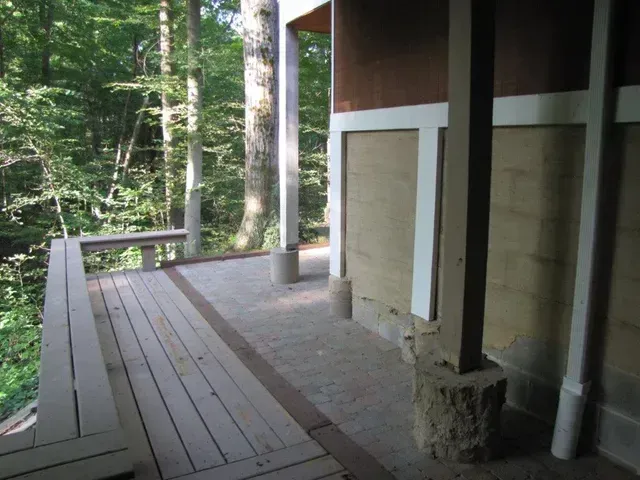 Wooden porch deck beside a forest, with railings and support columns