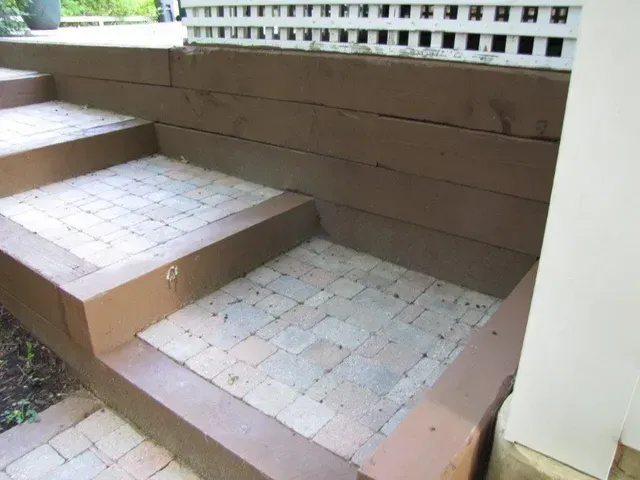 Brown tiled front steps leading to a small landing beside a house with white railing and siding