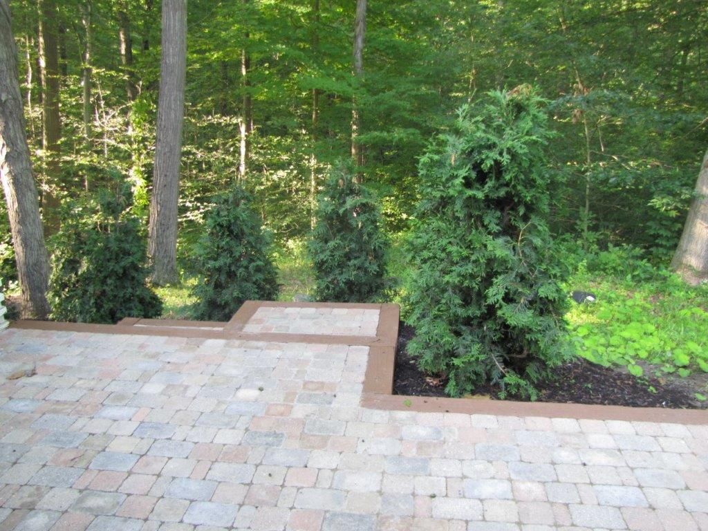 Paved patio with brick pavers beside a wooded garden and stone border