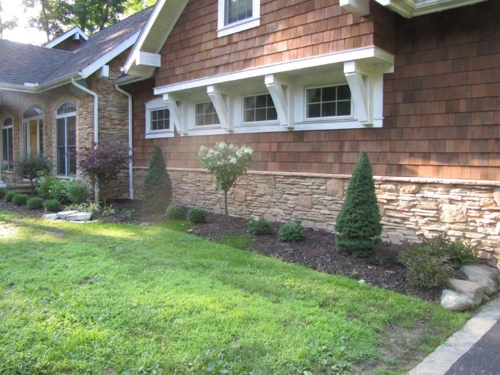Front yard of a house with green lawn, stone facade, shrubs, and a curved walkway
