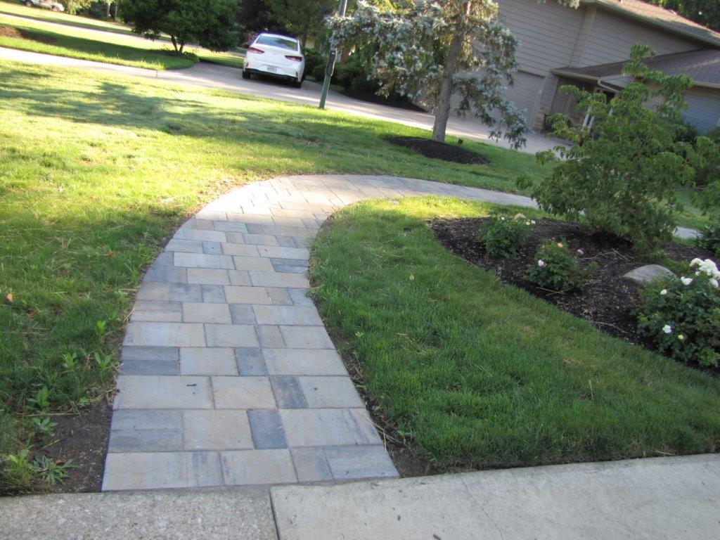 Stone walkway through a green yard toward a house, with a parked white car in the background