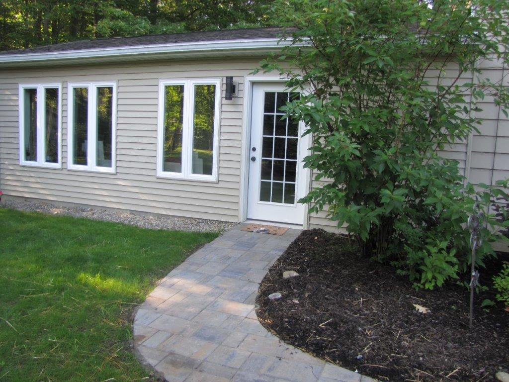 House exterior with white siding, front windows, and a paved walkway leading to a glass door