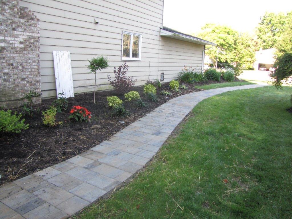 Curved stone walkway beside a house, with mulch beds and green lawn.