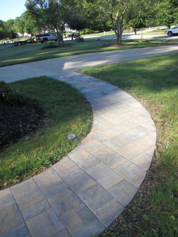 Curved light stone sidewalk through a green park lawn on a sunny day