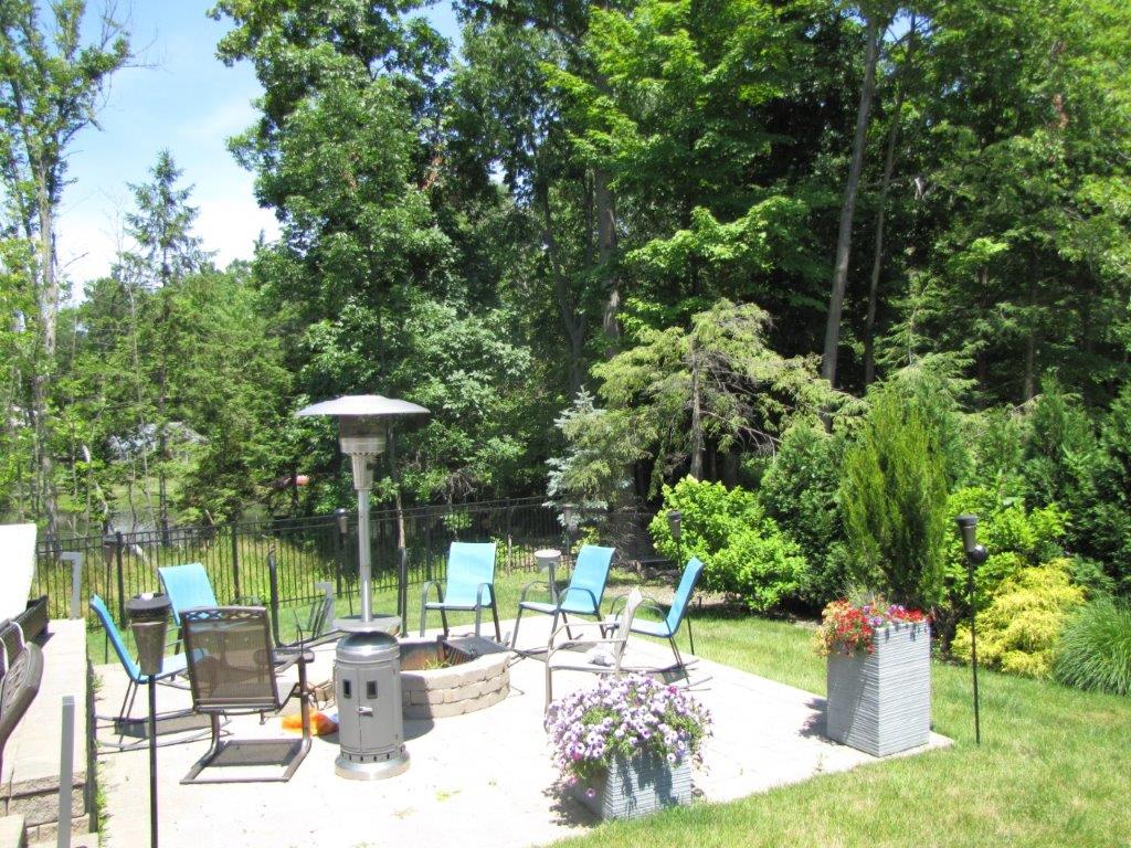 Backyard patio with lounge chairs, fire pit, and lush green garden in sunlight
