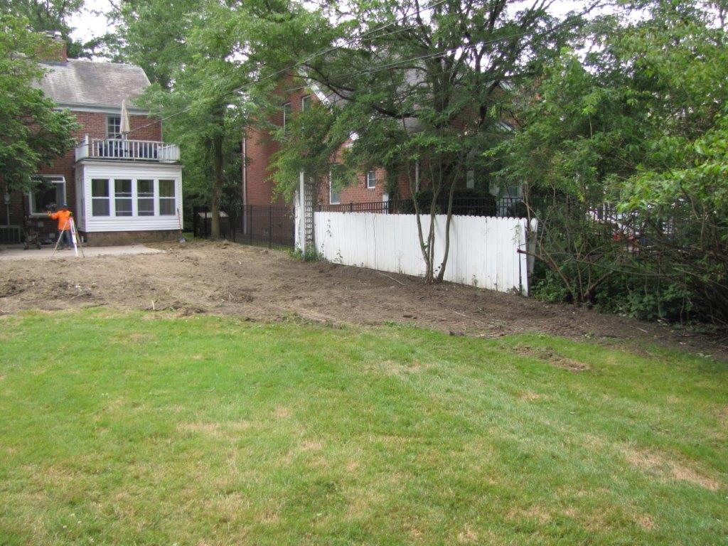 Backyard with grassy lawn, dirt patch, white fence, and house in the background