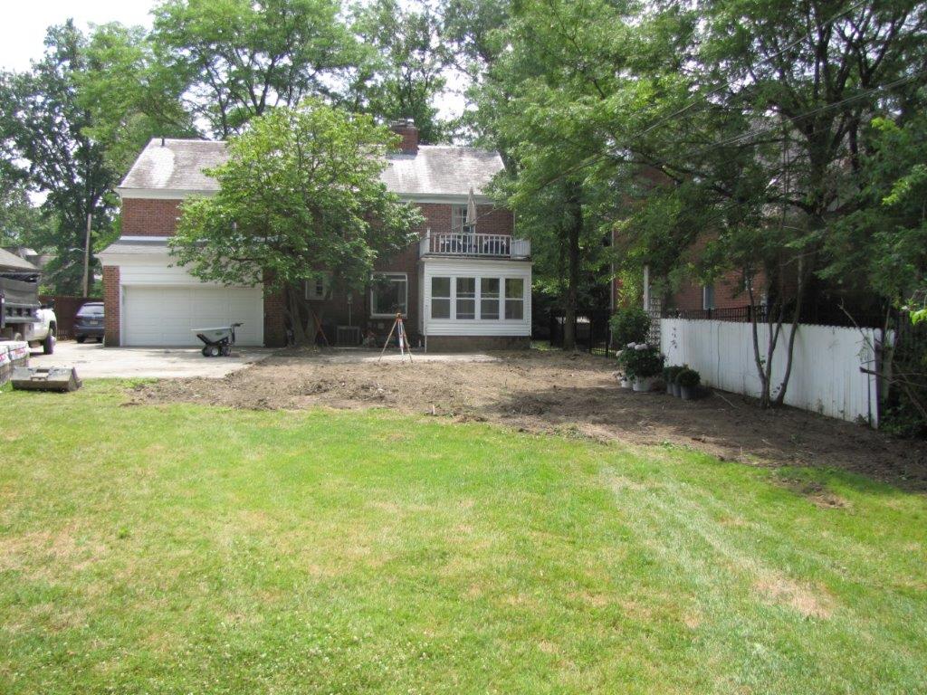 Suburban house with large front lawn, trees, and a white fence along the side yard