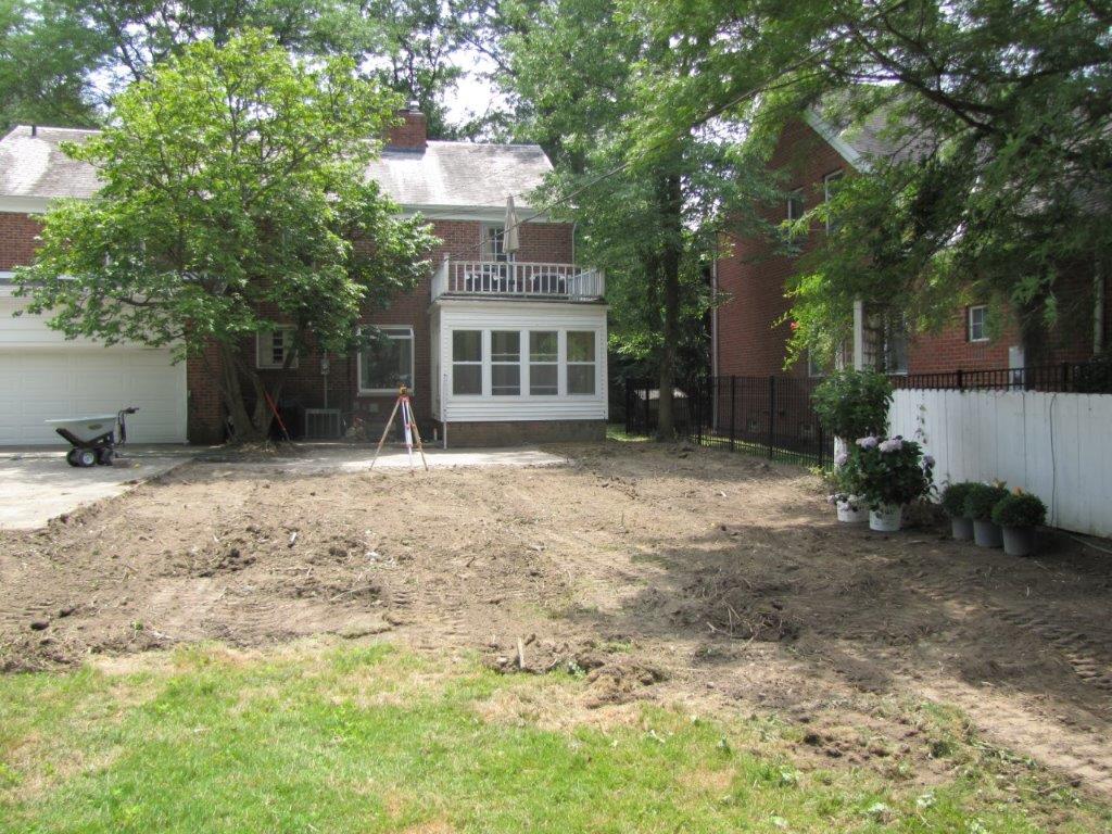 Backyard with bare dirt, green trees, and a house with a screened porch in the center.