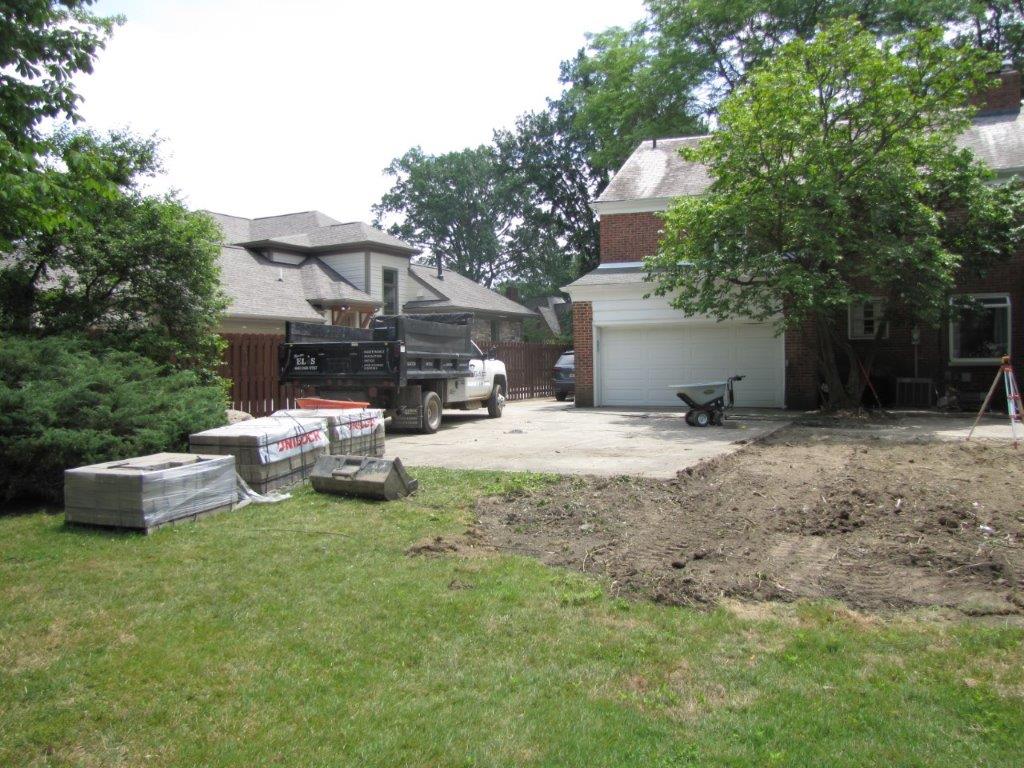 Backyard with a dirt patch, green lawn, trees, and a house garage in the background